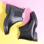 Black leather Block Heeled Chelsea Boots with elastic side panels and chunky soles against pink and yellow background
